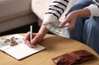 © New Africa - Pension and money savings. Senior woman with dollar banknotes and coins writing on notebook on sofa at wooden table, closeup