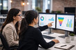 © hr-gold - Two businesswomen collaborate analyzing data presented on dual computer monitors