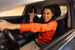 © Home-stock - Young woman driving car with playful expression, pointing upward while smiling