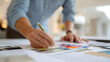 © A2Z AI  - Professional designer selects colors for a new project, working with swatches and a pencil, focus on hand and palette in a bright office environment