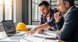 © Design - Construction Team Reviewing Plans on Laptop with Hard Hat in Office Collaboration and Teamwork in Building Project Development Strategy