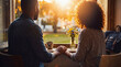 © Sarah - Young couple holding hands at a cafe window, enjoying a sunlit, intimate moment together, feeling connected.