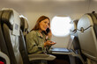 © SISMIZ - Woman talking on phone, working on laptop in airplane