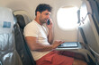 © SISMIZ - Man talking on phone, working on laptop during airplane flight