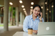 © Tj - Young Asian businesswoman multitasking, having a phone call while typing on a laptop and enjoying coffee outdoors, representing a modern mobile office or distant work lifestyle