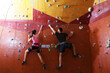 © New Africa - Athletic man and woman climbing wall in gym, back view
