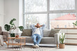 © Pixel-Shot - Young man resting on sofa near large window at home