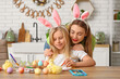 © Pixel-Shot - Cute little girl and her mother in bunny ears painting Easter eggs in kitchen