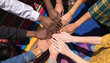 © Hamza - Diverse group of people from different ethnic backgrounds putting their hands together in a symbol of unity and teamwork on a colorful fabric