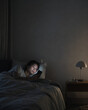 © Sukifli Dakheng - Young woman lying in bed feeling relaxed using smartphone