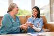 © Iryna - Senior woman receives care and advice from nurse during home visit in a sunny living room setting