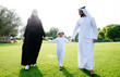 © oneinchpunch - Arab family, a father, mother, and young son, walking across a green park lawn holding hands, symbolizing happiness, parenthood, togetherness, and a loving childhood outdoors