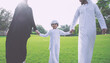 © oneinchpunch - Arab family, a father, mother, and young son, walking across a green park lawn holding hands, symbolizing happiness, parenthood, togetherness, and a loving childhood outdoors