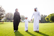 © oneinchpunch - Arab family, a father, mother, and young son, walking across a green park lawn holding hands, symbolizing happiness, parenthood, togetherness, and a loving childhood outdoors