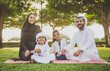 © oneinchpunch - Arabian family in traditional dress smiling together on a picnic blanket in a sunny green park, parents and children enjoying leisure, bonding and relaxation outdoors