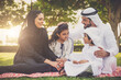 © oneinchpunch - Arabian family in traditional dress smiling together on a picnic blanket in a sunny green park, parents and children enjoying leisure, bonding and relaxation outdoors