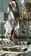 © Zaiteva Irina - Woman in flowing dress walking up modern wooden stairs at home, elegant lifestyle movement in minimalist interior with copy space