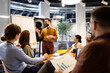 © littlewolf1989 - Business professional leading meeting presentation on whiteboard, sharing ideas with diverse team in modern office