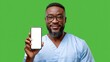 © Nick Freund - Ein lächelnder afroamerikanischer Krankenpfleger hält ein Smartphone mit weißem Bildschirm vor grünem Hintergrund.