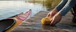 © Zaleman - Hands cleaning a wet wooden dock with a yellow sponge beside a kayak on calm lake water, with reeds and soft sunlight near shore outdoors