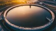© Kristina - Water treatment facility shows round tank at sunset with reflections on surface and surrounding industrial area