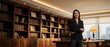 © Yuliia - Confident professional woman in a dark suit stands arms crossed in an elegant executive office with bookshelves and city view.