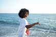 © SISMIZ - Joyful curly-haired woman dancing along the sunlit ocean shore on a beautiful sunny day