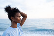 © SISMIZ - Young woman with dark curly hair in a bun looks out at the ocean