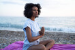 © SISMIZ - Woman meditating on a beach with hands in prayer pose by the ocean