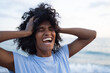 © SISMIZ - Joyful woman with curly hair laughing with eyes closed by the ocean