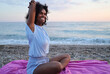 © SISMIZ - Woman practicing yoga on a pebble beach at sunset with ocean waves in the background