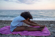 © SISMIZ - Woman stretching on a beach towel by the ocean at sunset