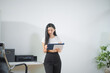 © laddawan - Asian businesswoman working from home on a cozy sofa, reviewing documents in a modern living room with a comfortable remote work lifestyle vibe.