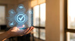 © Mk Design store - Quality assurance and standard compliance concept. Hand holding a glowing virtual checkmark hologram with business process icons in a modern office.