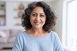 © Khawla - Confident Mature Woman Smiling at Home. portrait of a senior latina woman with gray hair sitting in a living room with a potted plant in front at home