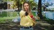 © Krakenimages.com - Woman points finger at camera while holding red heart and visitor badge in park; compassion volunteer care.