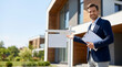 © Alena - Male real estate agent in a suit presenting a blank sign in front of a modern house with a landscaped yard and clear blue sky in the background