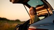 © MDMasud - Happy young woman sitting in the trunk of a car enjoying a beautiful sunset during a summer road trip