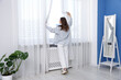 © New Africa - Woman in shirt opening beautiful window curtains at home