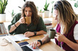 © Studio Marmellata - Two women are working together at a table, one is typing on a laptop and the other is drinking from a mug.