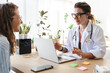 © Studio Marmellata - A doctor in a white coat consults with a patient, using a laptop and notes to discuss medical information in a bright, modern office setting.