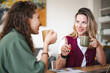 © Studio Marmellata - Two women are having a conversation over coffee at a table, one gesturing with her hand while holding a mug.