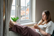 © Cavan - Exhausted woman sitting by window with coffee at home
