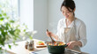 © Blue Studio - 明るいキッチンで笑顔で煮込み料理を作るエプロン姿の若い女性