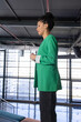 © wavebreak3 - African American woman standing in profile at modern atrium with grid windows, wearing green blazer