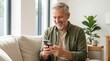 © StockSphere - Smiling happy senior mature middle aged man holding cell mobile phone using smartphone sitting at home on couch, scrolling social media, checking financial apps, buying online, texting messages.