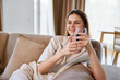 © SHOTPRIME STUDIO - Woman smiling on couch at home holding a glass of water, relaxed and comfortable in casual loungewear, natural light in a cozy livingroom scene conveying calm and wellness.