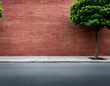 © Kursi - A vibrant red brick wall stands adjacent to a paved sidewalk and a quiet asphalt road, with a neatly trimmed green tree adding a touch of nature to the urban scene.
