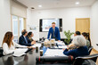 © Koldo_Studio - Business leaders holding a meeting in an office, discussing construction project plans and architectural models with a male presenter