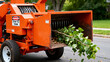 © NaesyaStudio - Powerful industrial wood chipper machine actively processing fresh tree branches, transforming foliage into organic chips for landscaping and clearing projects